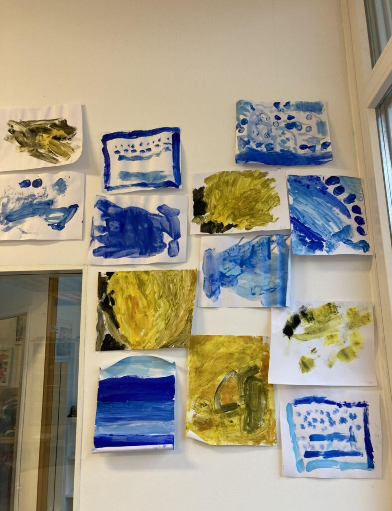 Mit Wasserfarben gemalte Bilder, die an der Wand hängen. Unterschiedliche Farbabstufungen der Farbe Blau und gelbe Bilder mit dunklen Nuancen.