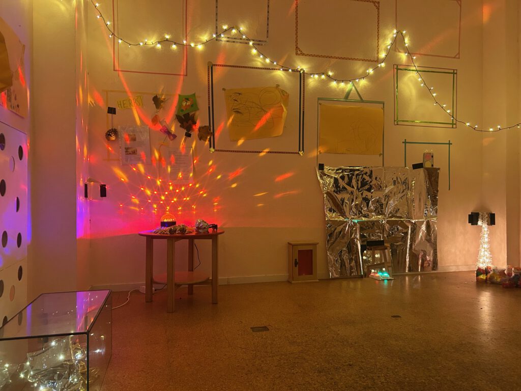 Lichtinstallation. Korfußboden, darauf ein Tisch  und künstlerische Gegenstände sowie viele kleine Leuchten hauptsächlich in Rot und Cremeweiß